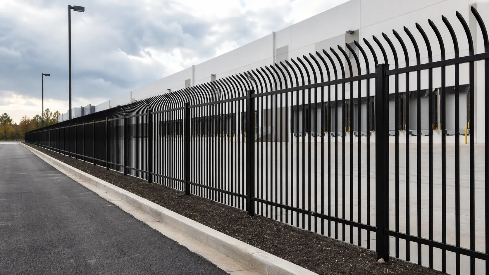 bent top metal security fence installed along industrial warehouse perimeter